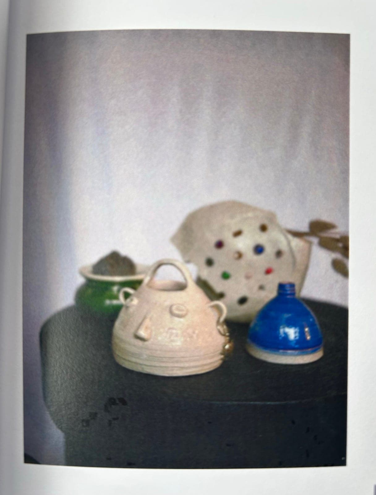 A cream lidded jar with a face, a blue lidded pot, a green bowl and a white vessel set with coloured glass