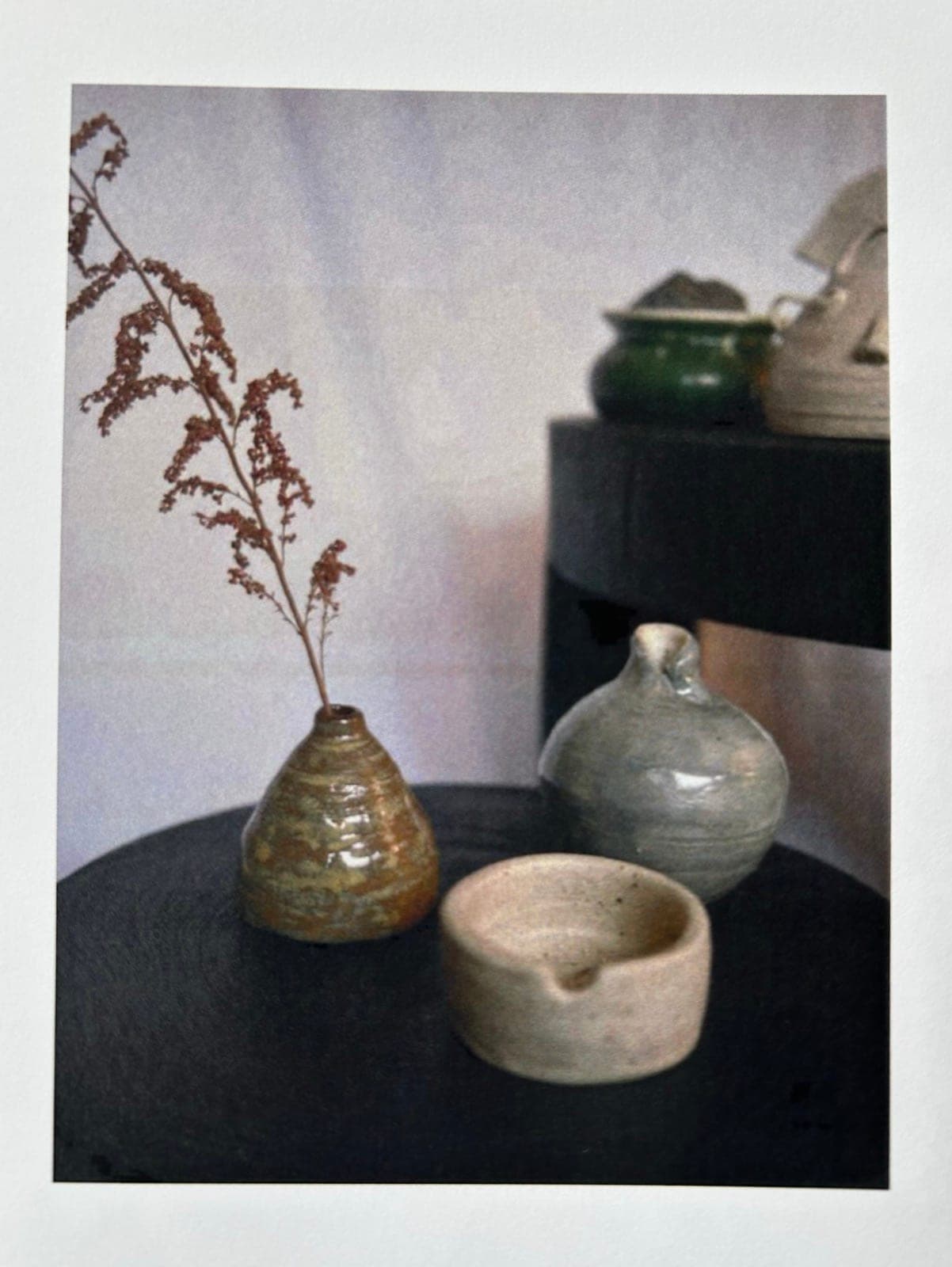 A ribbed brown bud vase with dried grasses, a grey bottle and a small cream bowl