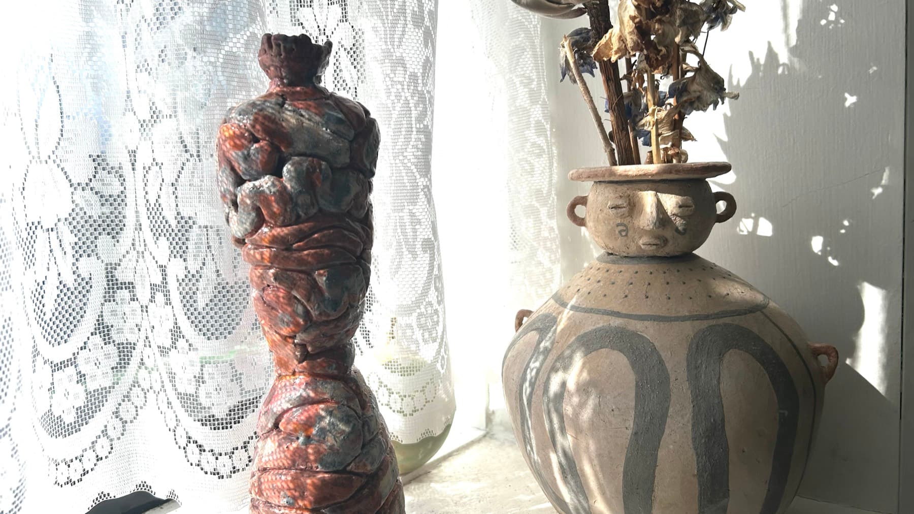 Two hand-built ceramic vessels on a windowsill in hard sunlight